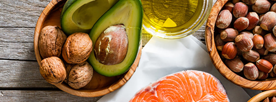 Healthy fats including avocado, walnuts, hazelnuts, olive oil and fresh salmon on a wooden table – SANUSq Health