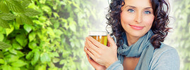 Smiling woman holding a cup of jiaogulan herbal tea against green leaves, an adaptogen for stress – SANUSq Health
