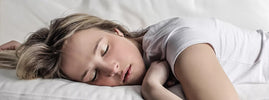 Young woman napping peacefully on white bedding, enjoying the benefits of a power nap – SANUSq Health