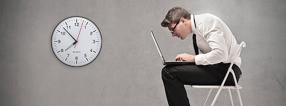 Man hunched over a laptop on a chair beside a wall clock, showing how sitting too long raises type 2 diabetes risk, by SANUSq Health
