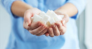 Woman holding a handful of white sugar cubes in cupped hands, showing why sugar is bad for your health – SANUSq Health